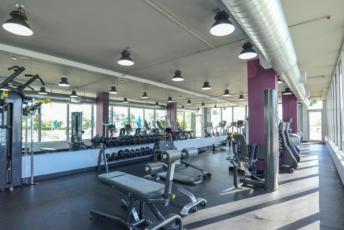 A gym with exercise equipment, mirrors, and a large window.
