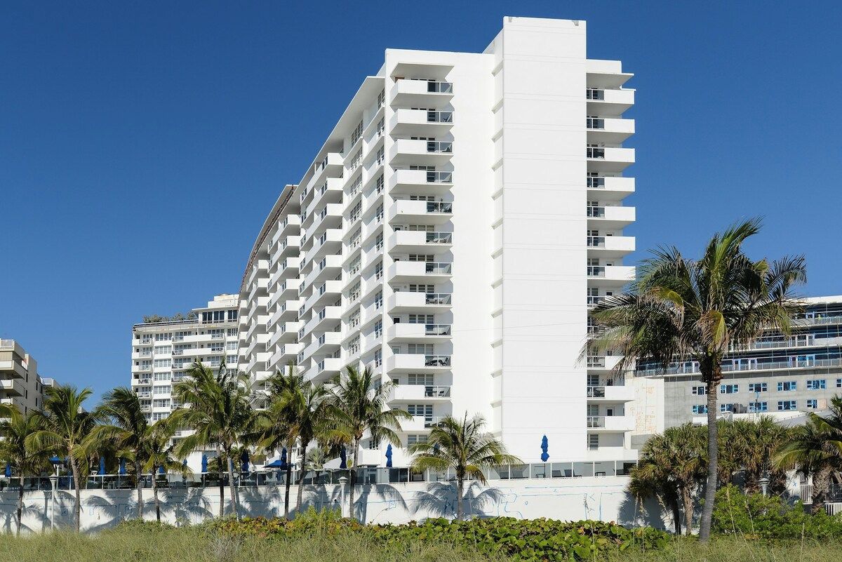 A multi-story hotel with balconies, palm trees, and a clear blue sky.
