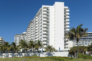 A multi-story hotel with balconies, palm trees, and a clear blue sky. - Decoplage Paradise - Unit A (Miami Beach)