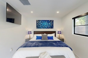 A modern bedroom with a bed, a wall-mounted TV, a painting, and a window. - The Favorite Place - Private Pool (Fort Lauderdale)