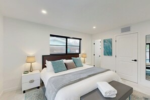 Ein modernes Schlafzimmer mit einem großen Bett, Nachttischlampen, einer Bank und Blick durch ein Fenster.
