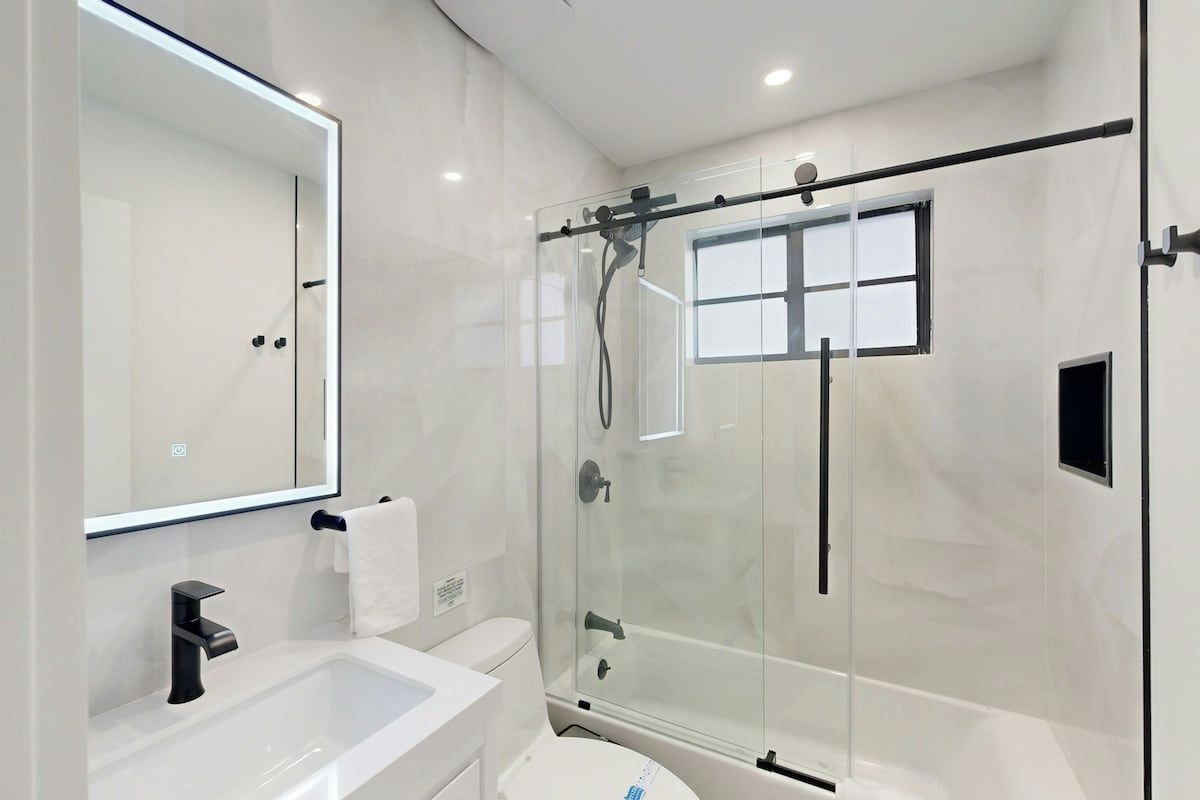 Un baño moderno con ducha de vidrio, lavabo blanco y un espejo grande.
