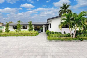 Ein modernes, zweigeschossiges Haus mit gepflasterter Auffahrt, umgeben von gepflegter Bepflanzung und Palmen.