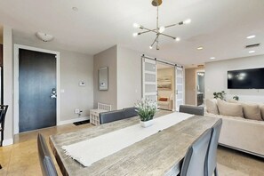 Ein modernes Wohnzimmer mit Essbereich, einer Couch, einem an der Wand montierten Fernseher und einer Deckenleuchte.