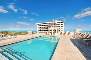 A rooftop pool with a clear view of the ocean, a multi-story building, and sun loungers. - Modern Ocean Drive Condo in the Heart of Sobe (Miami Beach)