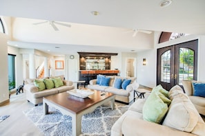 A spacious living room with a high ceiling, a central coffee table, and a kitchen area in the background. - Rustling Palms - Private Pool (Fort Lauderdale)
