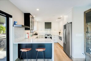 Een moderne keuken met een centraal eiland, barkrukken, roestvrijstalen apparatuur en witte kasten.