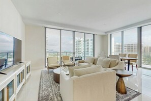 A modern living room with a large flat-screen TV, a sectional sofa, a coffee table, and a dining area with chairs. - Tranquil Tides - Beachfront (Riviera Beach)