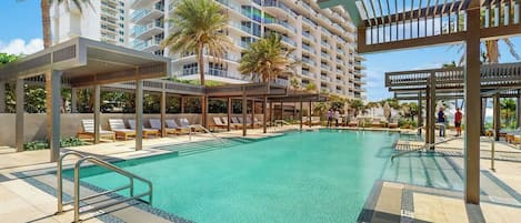 A swimming pool with lounge chairs and a covered area, surrounded by tall buildings.