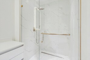 Een moderne badkamer met een douchecabine van glas, marmeren wanden en een wit aanrecht.