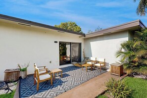Eine moderne Außenpatio mit einem gemusterten Teppich, Holzmöbeln und einem kleinen Gartenbereich.
