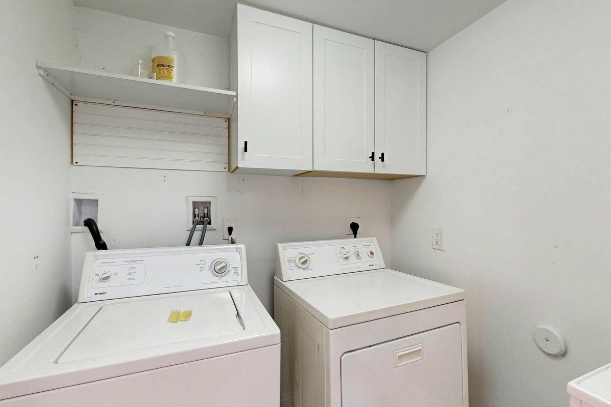 A laundry room with two washing machines and a shelf with a bottle.