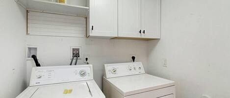 A laundry room with two washing machines and a shelf with a bottle.