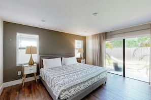 Ein Schlafzimmer mit einem großen Bett, zwei Nachttischen, einem Fenster und einer Schiebeglastür, die auf einen Balkon führt.