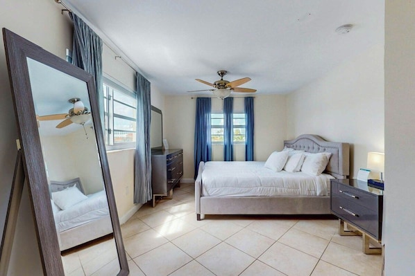 A bedroom with a bed, a dresser, a mirror, a ceiling fan, and a window with curtains. - Samira's South Beach Paradise (Miami Beach)