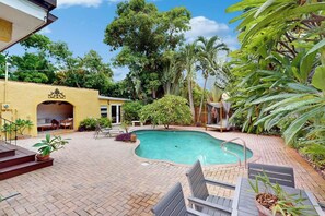 A swimming pool with a brick patio, surrounded by lush greenery and a yellow building. - Villa Sunset - Private Pool (West Palm Beach)