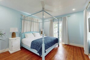 Une chambre à coucher avec un lit à baldaquin, une table de chevet, un ventilateur de plafond et une fenêtre avec des rideaux.