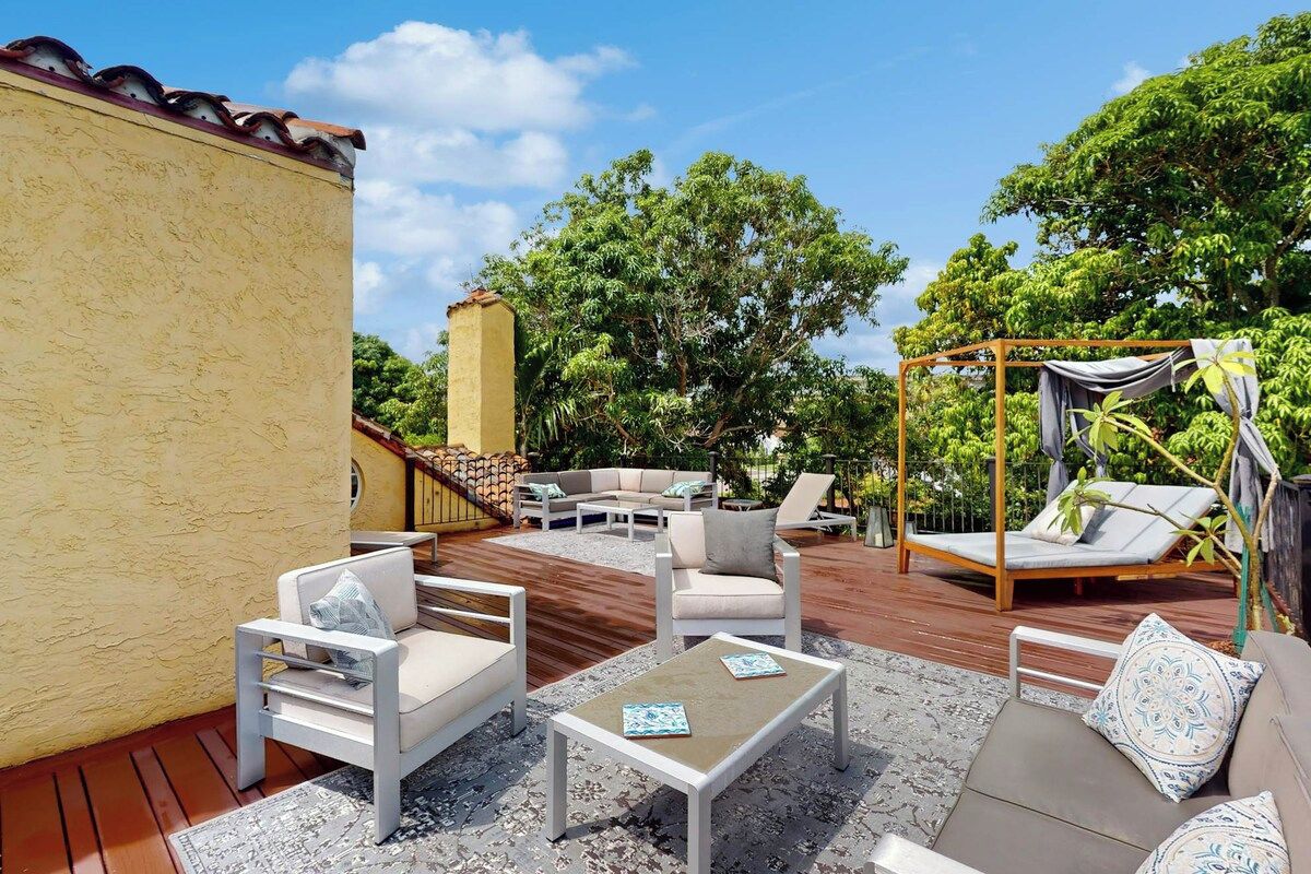 Une terrasse extérieure dotée d’une plateforme en bois, de mobilier blanc et d’une structure en forme de tonnelle.