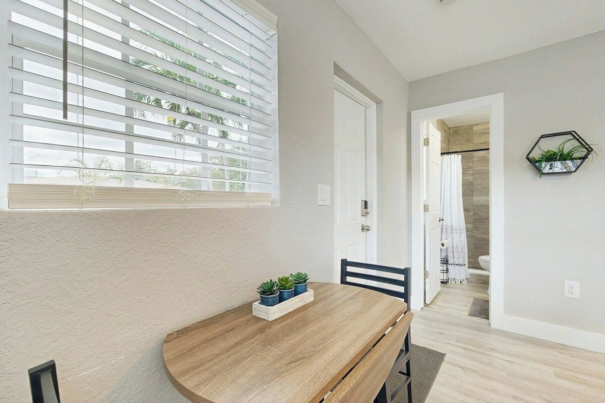 Un coin repas avec une table en bois, des plantes en pot et une vue sur la salle de bain adjacente.