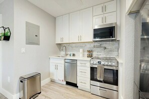 A modern kitchen with white cabinets, stainless steel appliances, and a tiled backsplash. - The Palms Unit 2 - Enclosed Yard (Fort Lauderdale)