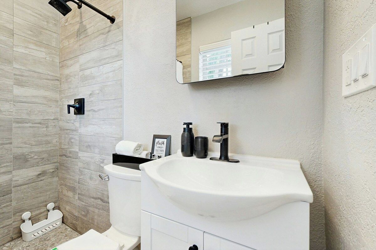 Un baño con lavamanos blanco, un espejo y cabina de ducha.