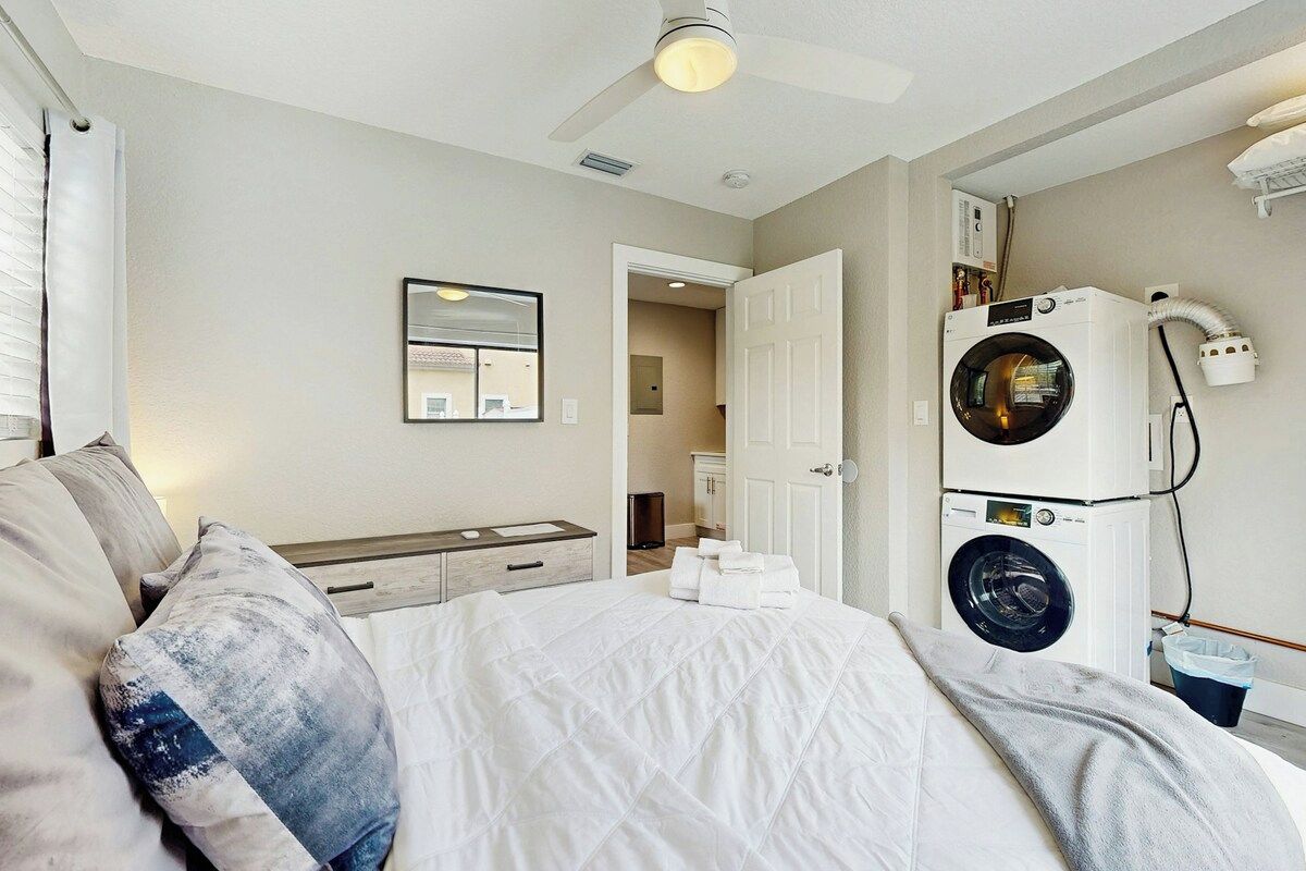 Een hotelkamer met een bed, een plafondventilator, een wasmachine en een spiegel.