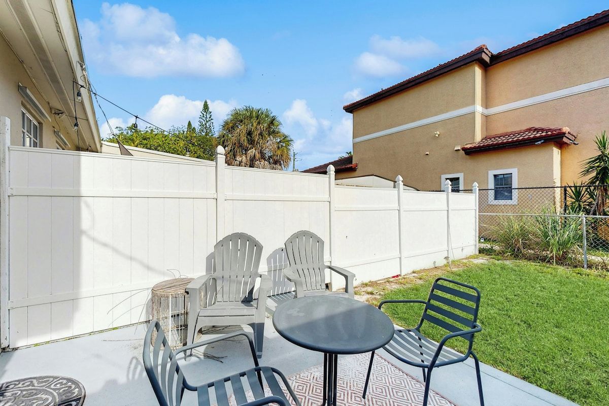 A patio with outdoor furniture, a white fence, and a building in the background.
