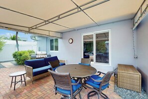 An outdoor patio with a round table, blue cushioned chairs, a blue sofa, and a wicker bench. - The Front House - Private Pool (Fort Lauderdale)