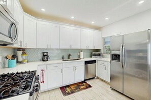 A modern kitchen with white cabinets, stainless steel appliances, and a tiled backsplash. - The Front House - Private Pool (Fort Lauderdale)