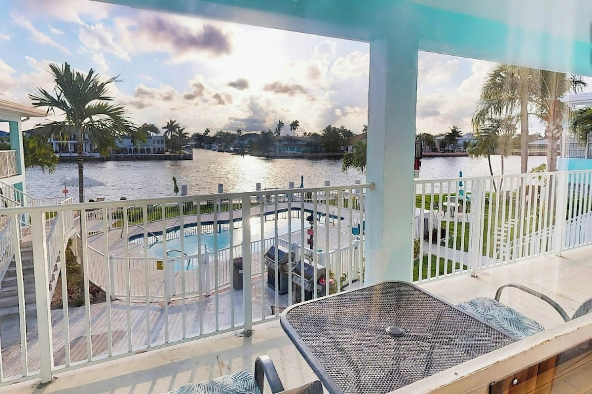 Varanda com vista para um corpo d'água, uma piscina e um muro branco.