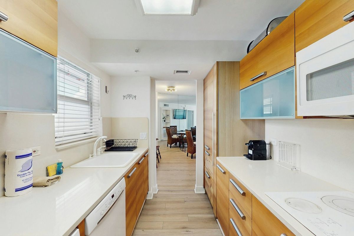 A narrow kitchen with wooden cabinets, a microwave, and a sink.
