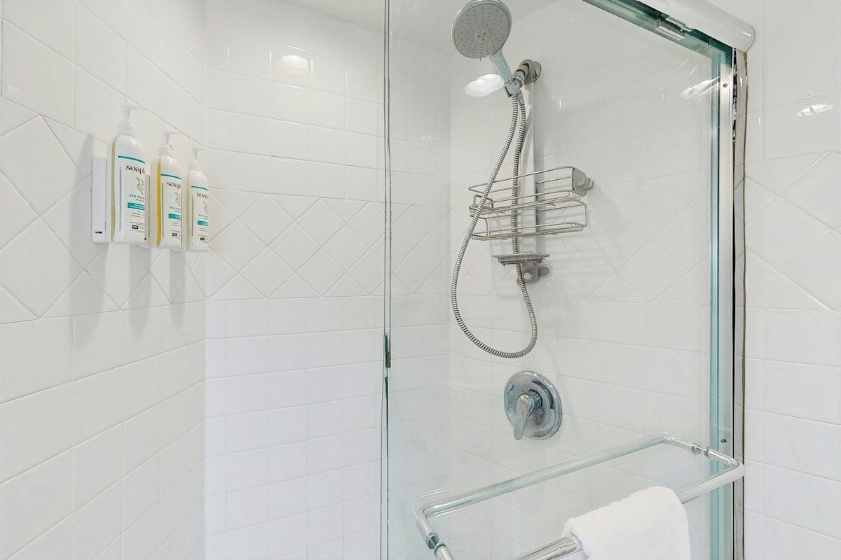 Una ducha moderna con cabina acristalada, cabezal de ducha manual y toallero de vidrio.