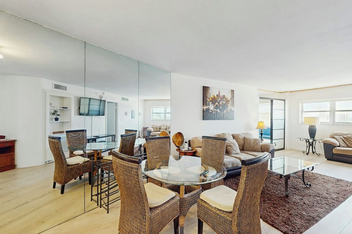 A modern living room with a glass dining table surrounded by wicker chairs, a sofa, and a coffee table.