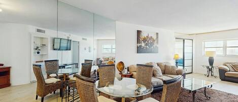 A modern living room with a glass dining table surrounded by wicker chairs, a sofa, and a coffee table.