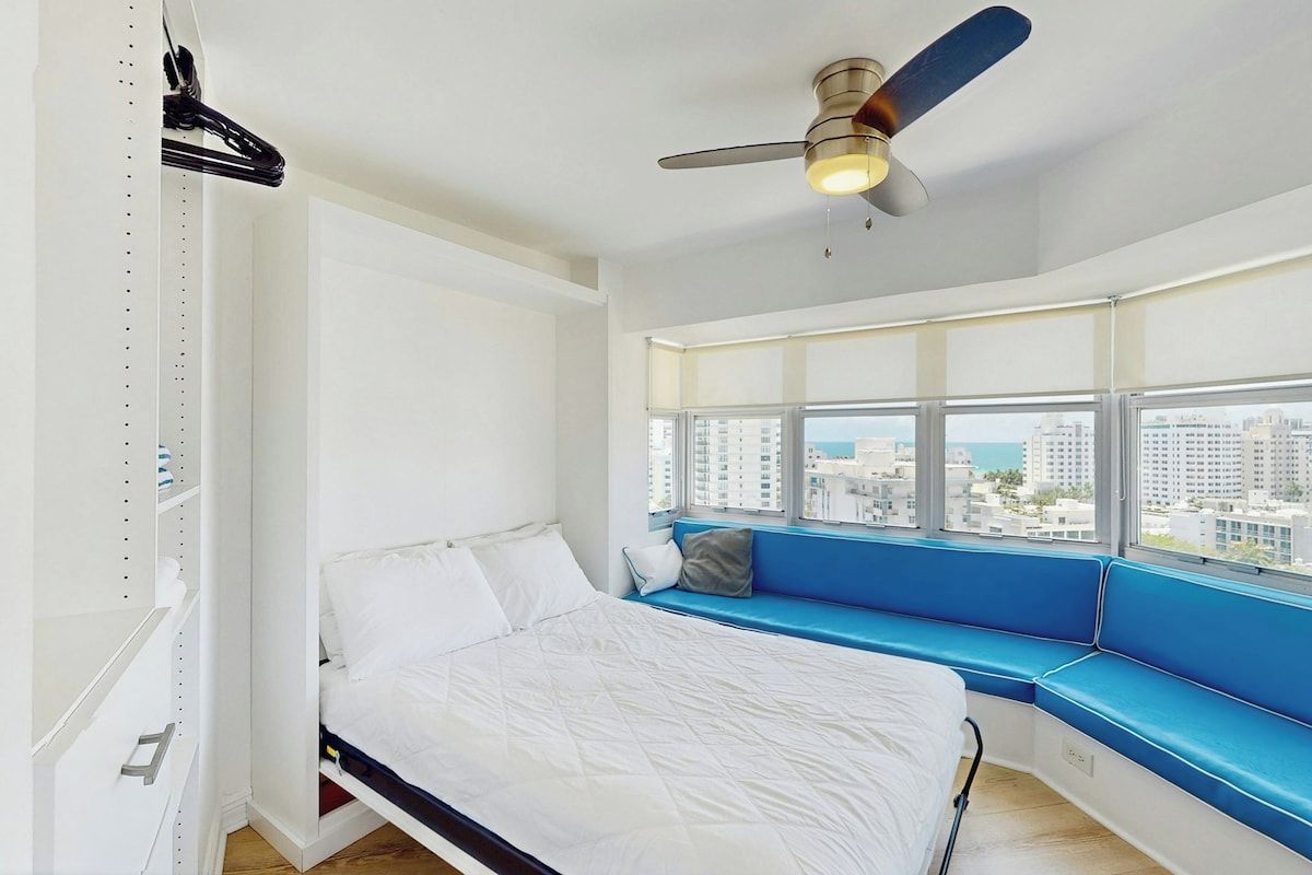 Een slaapkamer met een bed, een vensterbank, een plafondventilator en uitzicht op de stad.