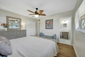 Een slaapkamer met een bed, een dressingkast, een kaptafel, een plafondventilator en een schilderij.