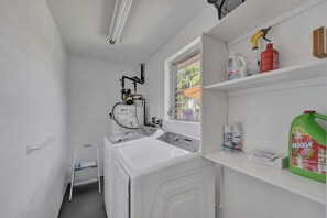 A laundry room with a washing machine, a drying rack, and shelves with cleaning supplies. - Tropical Bliss Alfresco Villa (Pompano Beach)