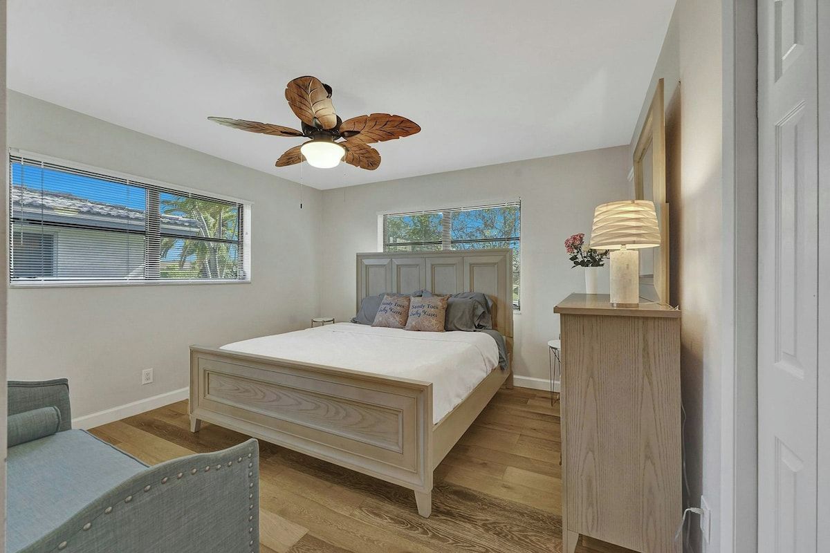 Quarto com cama, ventoinha no teto, janela e mesa de cabeceira.
