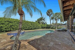 A swimming pool with a curved design, surrounded by stone tiles and palm trees. - Tropical Bliss Alfresco Villa (Pompano Beach)