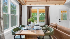 A dining area with a wooden table set for four, surrounded by green upholstered chairs, a bench, and a view of greenery outside. - Newly built private cabin with fire pit, Sauna. Close to National park entrance (Fort Valley)