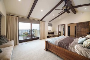 Ein Schlafzimmer mit einem großen Bett, einem Deckenventilator und Blick ins Freie durch eine Schiebetür.