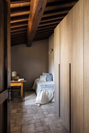 A bedroom with a wooden ceiling, a bed with a blue and white bedspread, a bedside table with a lamp, and a wall-mounted light fixture. - Gelsomina Country House - A historic farmhouse nestled in the peaceful Umbrian countryside (Umbria)