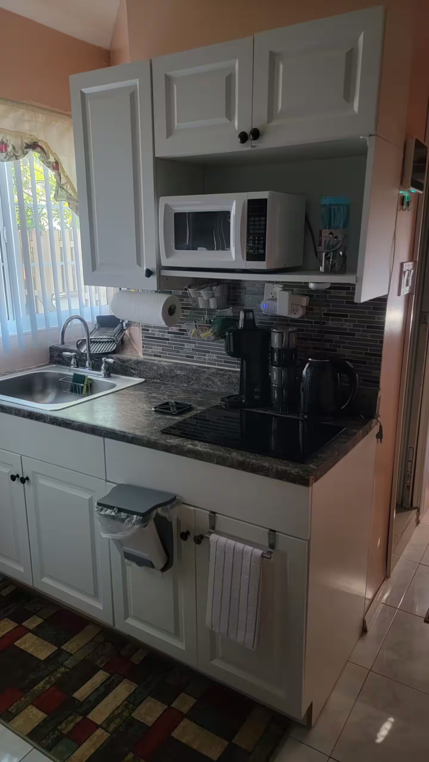 A kitchen with white cabinets, a microwave, a coffee maker, and a sink.