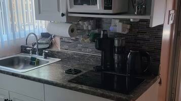 A kitchen with white cabinets, a microwave, a coffee maker, and a sink.