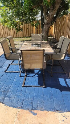 An outdoor patio with a table and chairs, surrounded by a wooden fence and a tree.