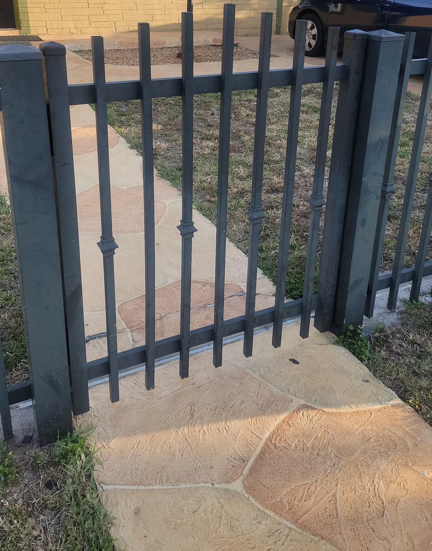 A metal fence with vertical bars and a stone pathway leading to a building.