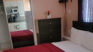 Un dormitorio con cama, cómoda, espejo y una kitchenette al fondo.