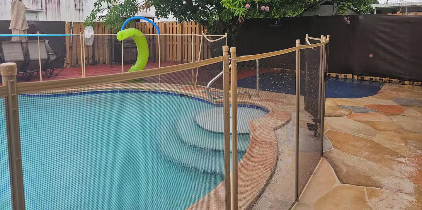 Una piscina interior con cerramiento de seguridad, un tobogán y suelo de baldosas de piedra.