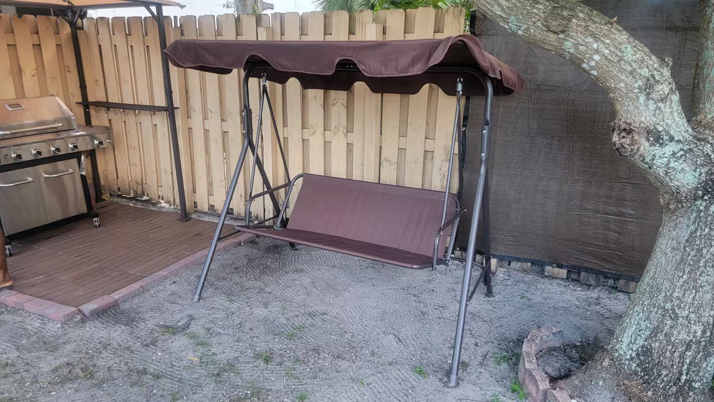 A patio area with a swing set, a grill, and a tree.