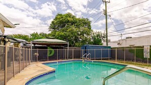 Una piscina con borde de azulejos, una zona de estar cubierta y una cerca delimitando el espacio.